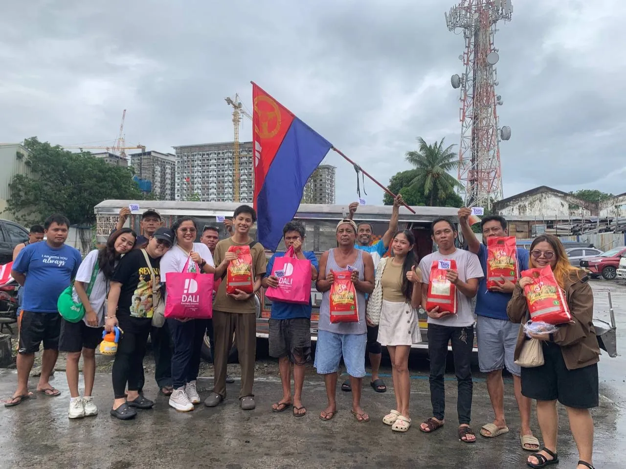 Volunteers and residents stand in a row outdoors holding relief packs, one of them raising a flag.